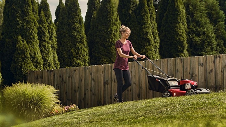 A woman pushing a Troy-Bilt mower uphill.