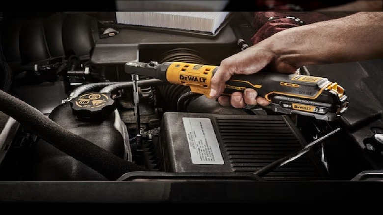 A mechanic using a DeWalt cordless ratchet to work on a car.