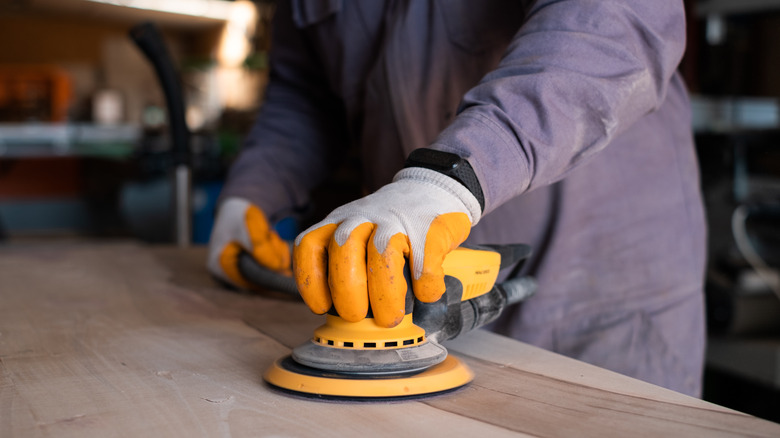 Person wearing yellow gloves using sander