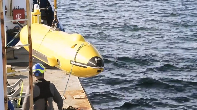 Sailors lowering an undersea drone into the water with a crane