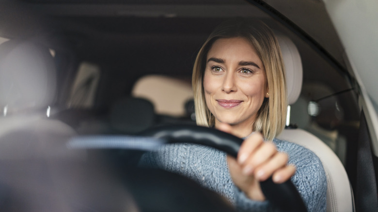 A blonde woman in a light blue sweater smiles while holding a steering wheel