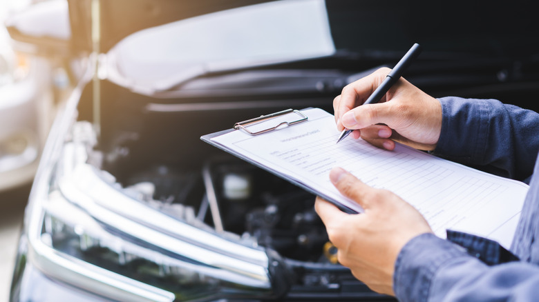 A technician holding a pen and paper while conducting a vehicle inspection