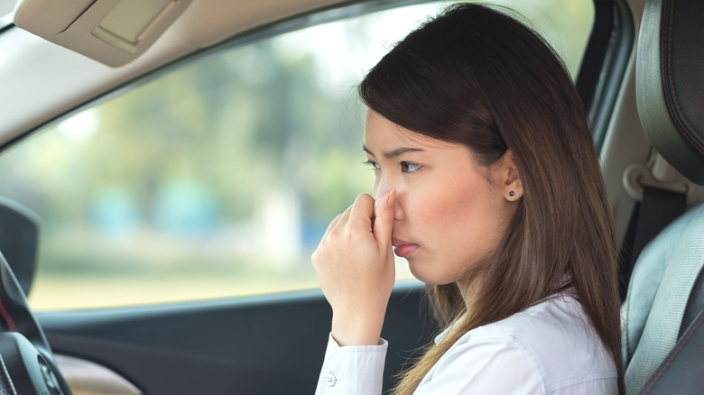 woman in car holding nose