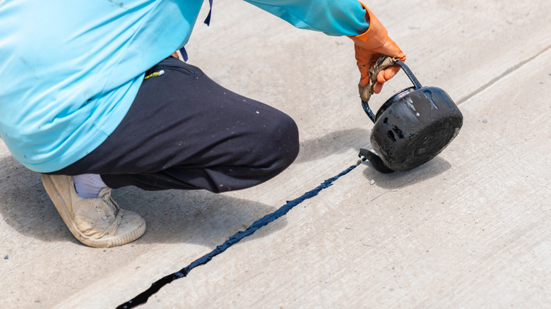 A person sealing a division in concrete with asphalt.