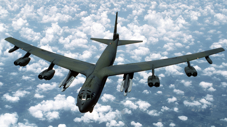 A B-52G armed with air-launched cruise missiles flying over broken clouds