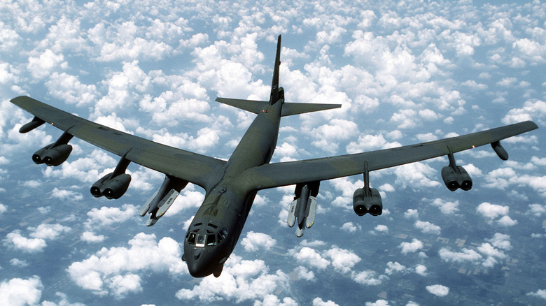 A B-52G armed with air-launched cruise missiles flying over broken clouds