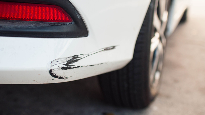 A close-up view of a white car with damaged rear bumper paint