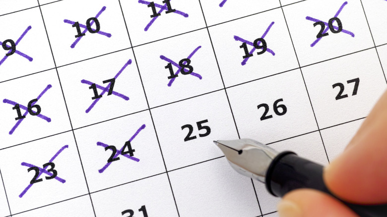 person marking days on calendar with pen