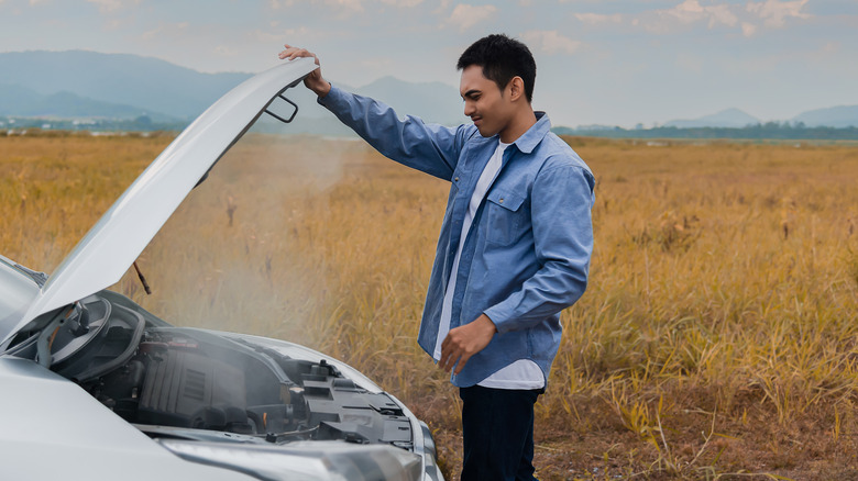 Man standing looking at overheating car in remote area