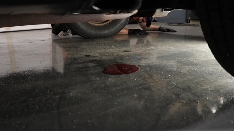 A person looking at a puddle of red fluid beneath their car