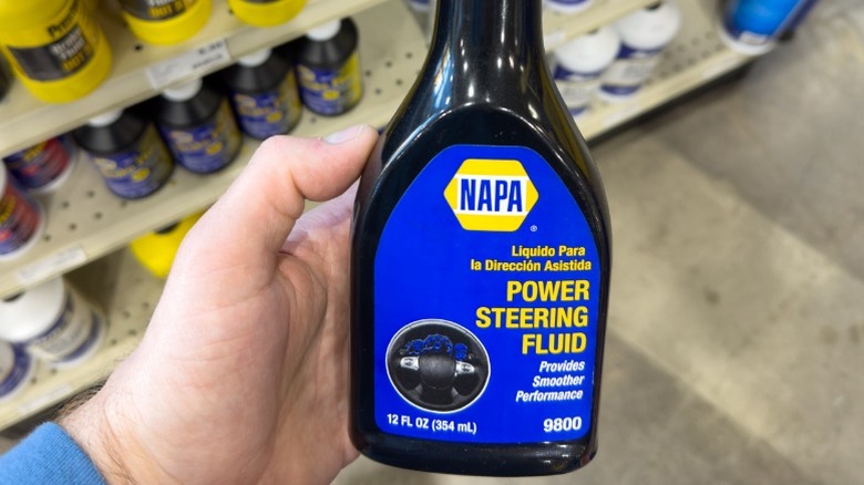 A person holding a bottle of napa-brand power steering fluid