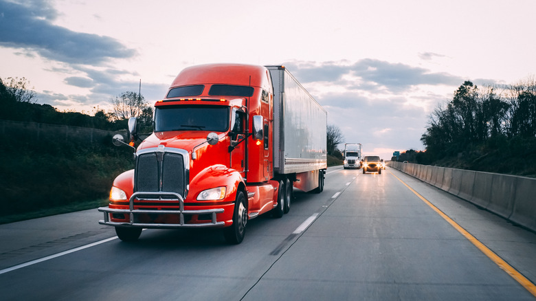 Orange red 18 wheeler new semi truck delivering goods on the road at night with headlights