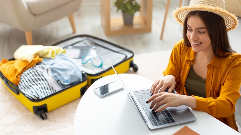 A person using their laptop while packing their bag for a vacation