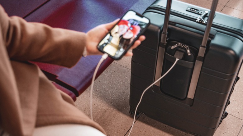 A person charging a smartphone using a power bank placed in a carry-on bag