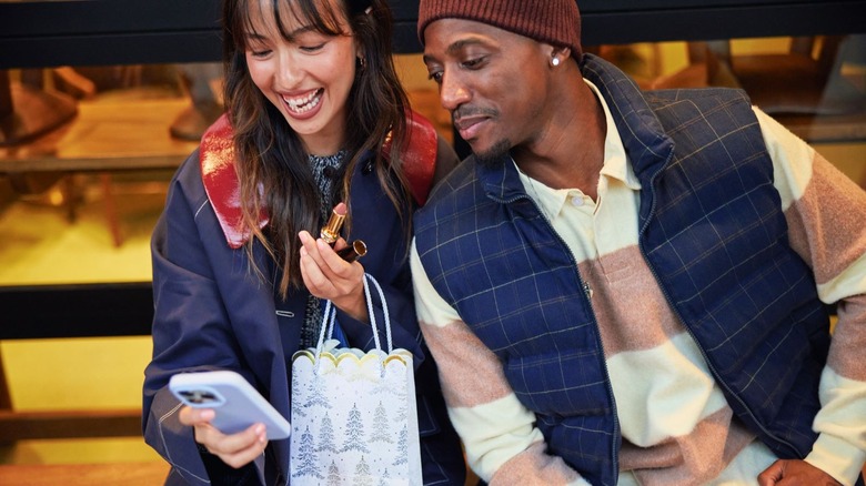 Two people smiling as they stare at a phone while shopping