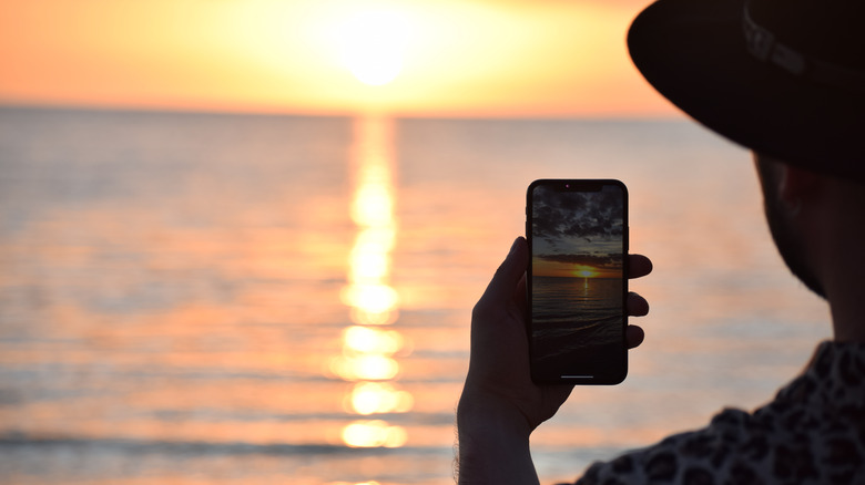 person taking picture of sunset on iPhone