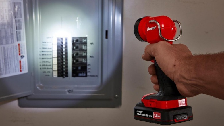 A person using a Bauer flashlight to see their circuit breaker box