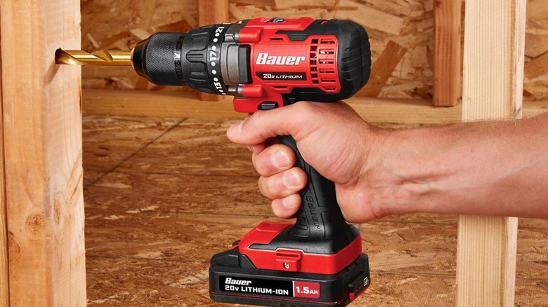 A person using a Bauer 1/2-inch drill/driver tool to drill a hole in a wood beam