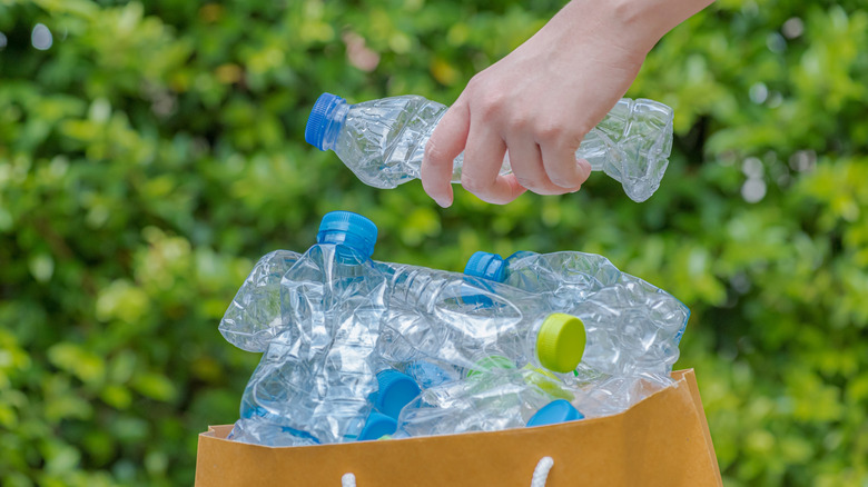 A hand placing an empty squashed plastic drinks bottle into a bag full of other empty plastic bottles