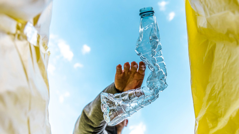 A man throws a plastic water bottle into a recycling bin