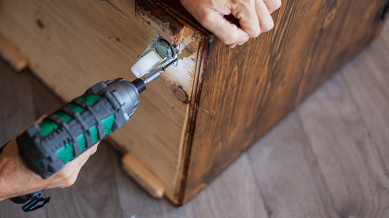 Using a drill to attach wheel to cabinet