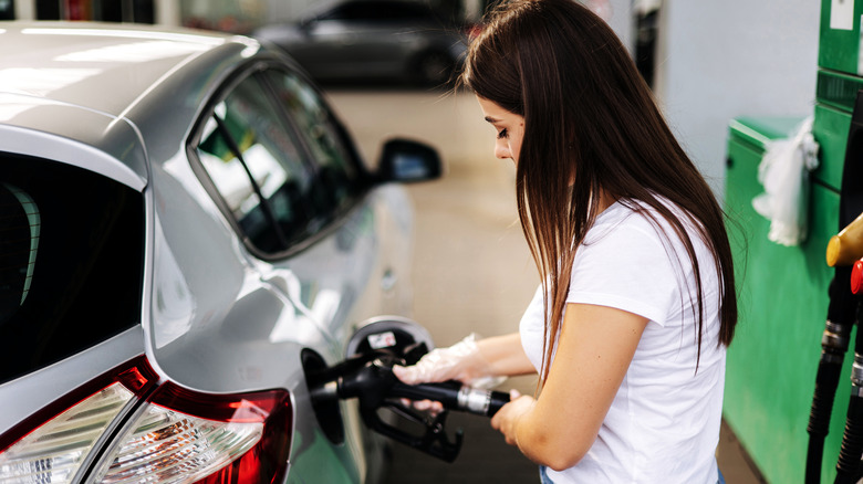 Woman pumping gas to gray vehicle