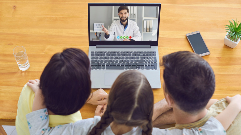 A group of people video chatting with someone on a laptop