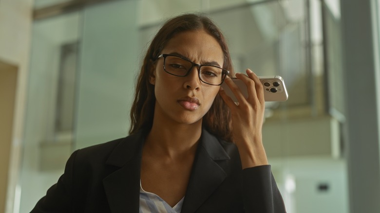 Woman looking serious while listening to voicemail on iPhone