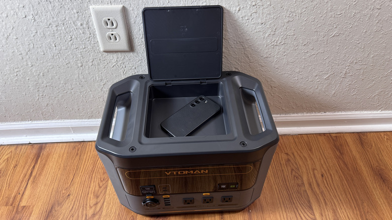 The VTOMAN FlashSpeed 1500 on a hardwood floor showing the top storage compartment with a phone inside.