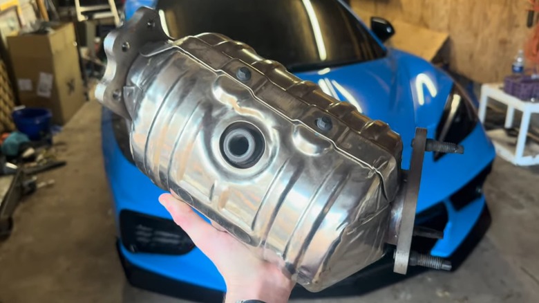 A person holding a catalytic converter in front of a blue car