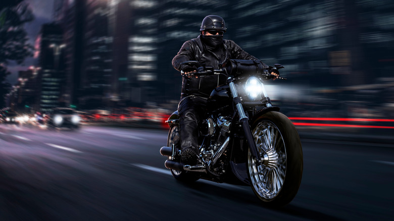 A biker in black leather riding chopper motorcycle downtown at night