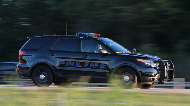 A zoomed in police vehicle with its siren on, driving along the highway.