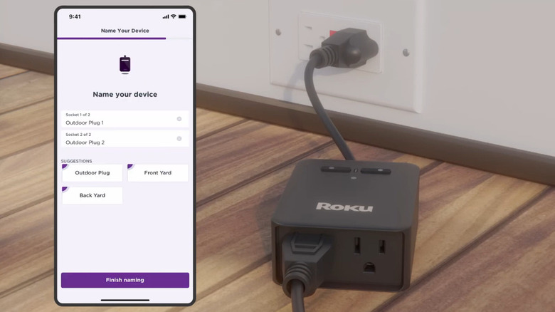 A Roku outdoor smart plug connected to a wall socket and getting set up via smartphone