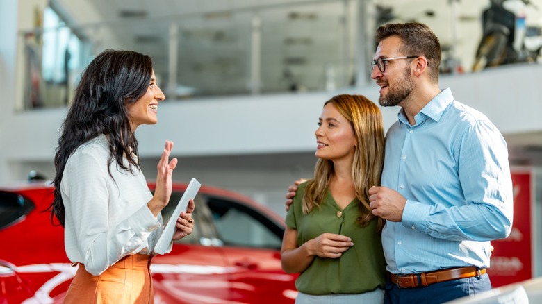 A salewoman at a car dealership talking to a couple who are prospective buyers.