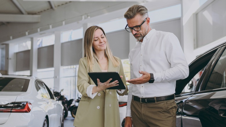 A woman at a dealership showing a prospective buyer some information