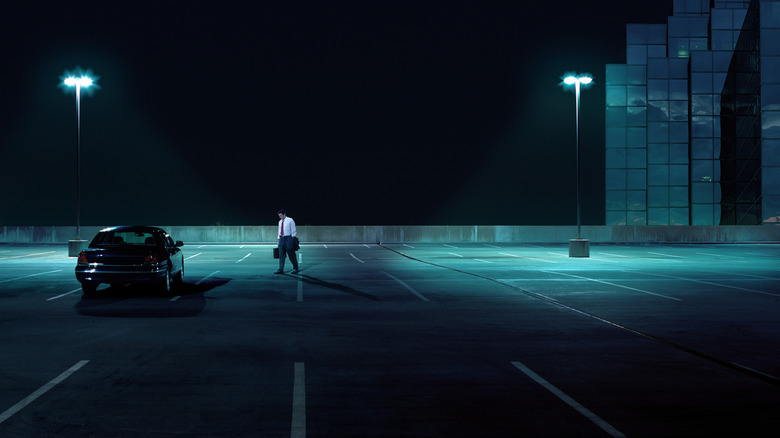 Person walking to car in empty parking lot at night.