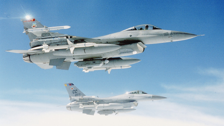 Two F-16 military jets flying against a slightly cloudy sky.