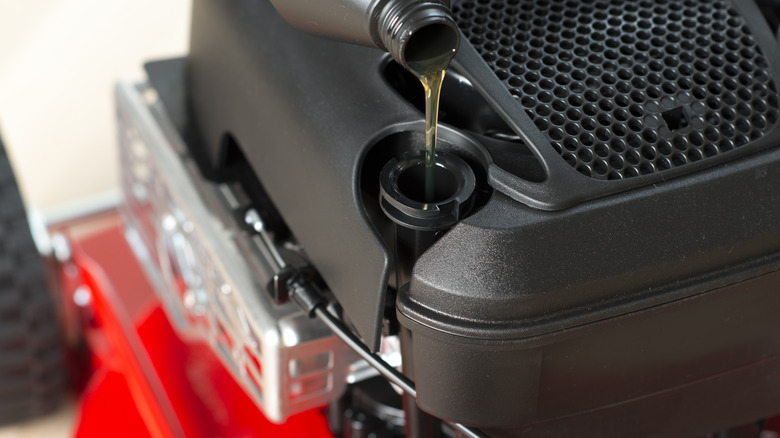 Person pouring oil in mower