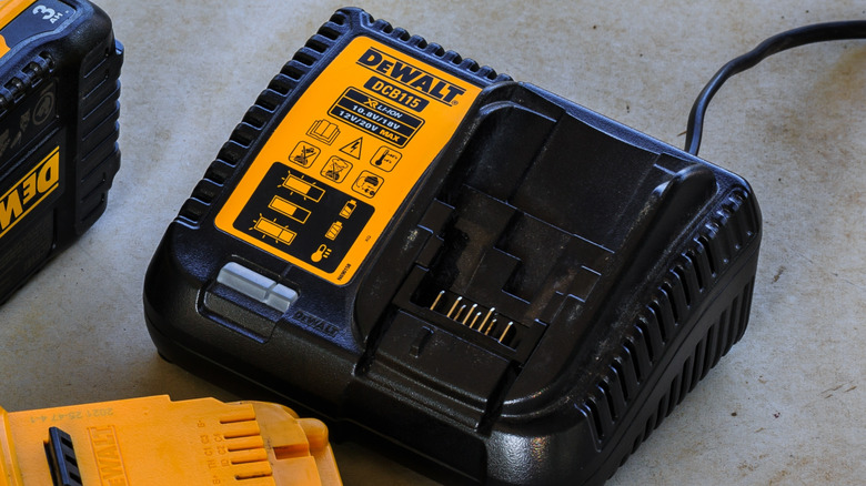 A DeWalt DCB115 battery charger placed on the ground beside the removable battery units of power tools