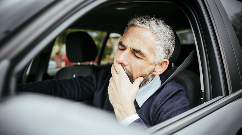 A tired driver covers up a yawn behind the wheel