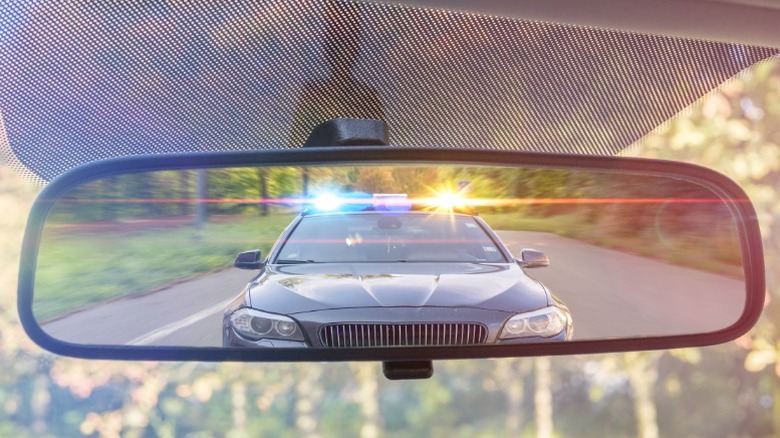 A picture of a car's rear view mirror showing a cop about to pull the driver over