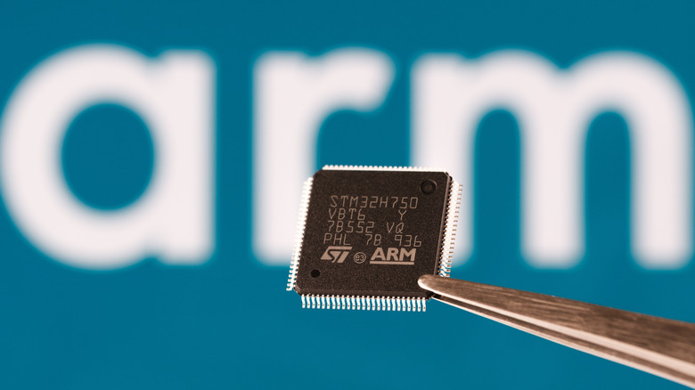 STM32 microchip held in tweezers with ARM logo in background.