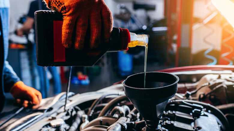 Close up hand of auto mechanic technician replacing and pouring motor oil in modern automobile engine at auto repair service station.