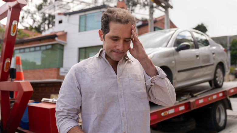 Worried man checks his phone as his car is towed away