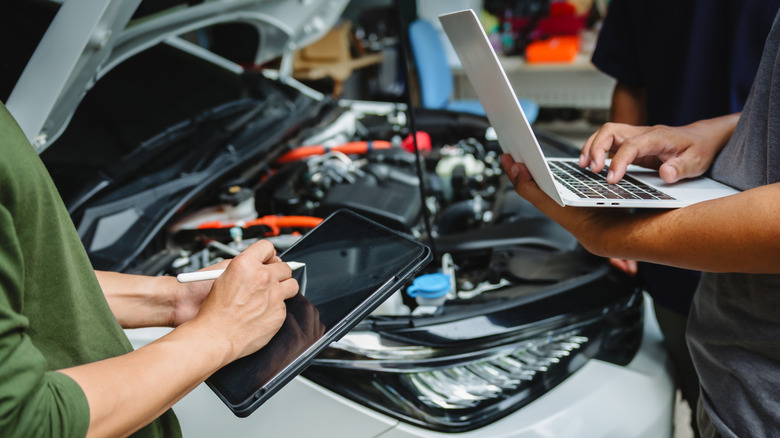 Three people check the components of a car in a mechanic shop