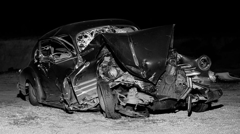 A smashed and totaled vintage car on the side of the road