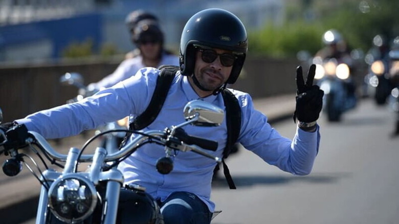 A biker holding up two fingers while riding his cruiser bike.