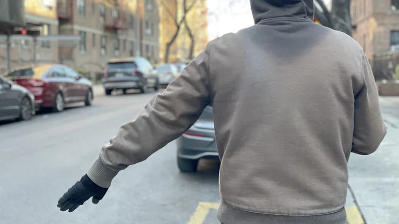 A man standing on side of a road with his left palm facing downward.