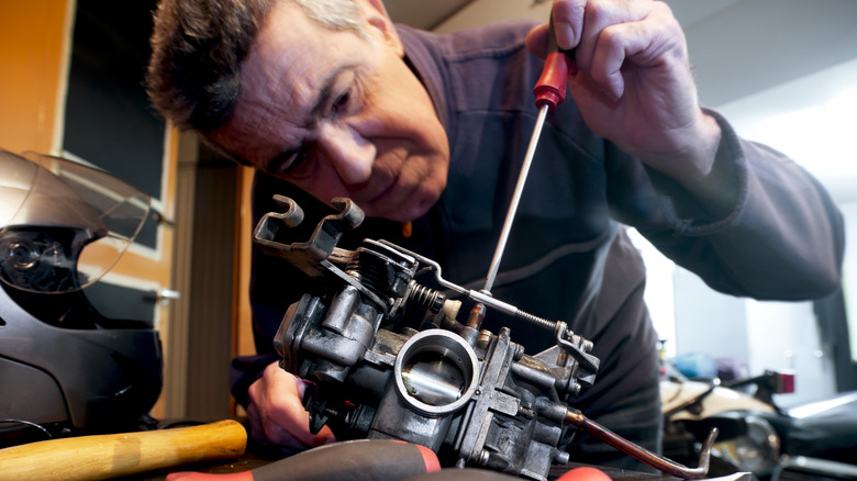 man adjusting mixture screw on motorcycle carburetor