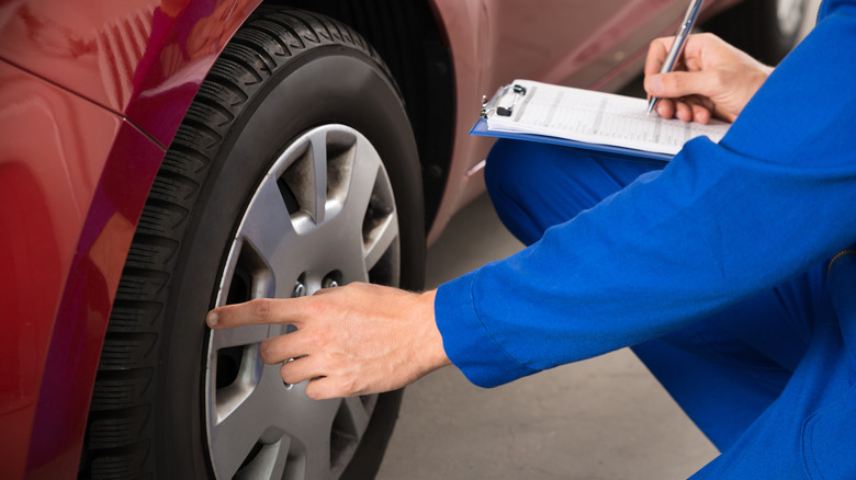 Mechanic Writing On Clipboard White Examining Car Wheel